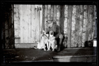 Portraits du Corps des forestiers canadiens et autres troupes : officier du 165e bataillon canadien enlaçant deux chiens devant un baraquement en bois.