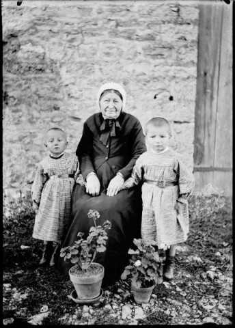 Une femme âgée avec deux enfants avec deux pots de géranium au premier plan