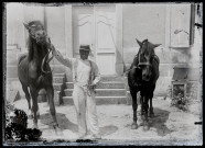 Portrait d'un homme tenant deux chevaux, devant les marches du pensionnat de jeunes filles rue du Tatet à Vers-en-Montagne.