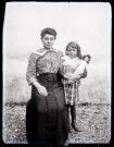 Portrait d'une femme assise serrant contre elle une petite fille tenant une poupée dans les bras.