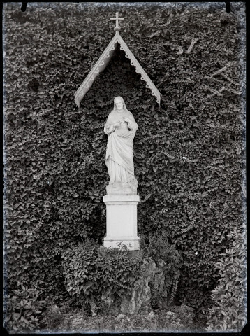 Statue du Christ, devant un mur de végétation.