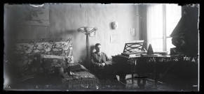 Jeune homme assis dans un intérieur décoré, près d'un piano.