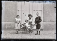 Portrait de deux filles et un garçon tenant des jouets entourant une petite fille assise dans une charrette.