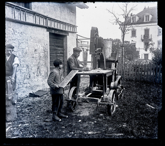 Homme et enfant utilisant une scie à ruban pour débiter des buches de bois.