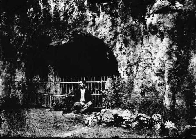 Un homme assis devant une grotte
