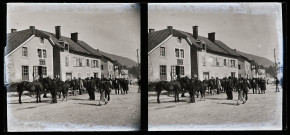 Groupes d'hommes et de chevaux dans une rue, devant des bâtiments.