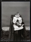 Portrait d'un petit enfant en robe rayée assis sur une chaise, un chaton dans les bras.