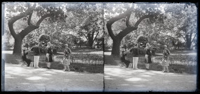 Trois femmes et un homme sous un arbre dans un parc, une statue émerge des buissons.
