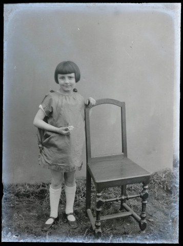 Portrait d'une fillette debout, appuyée à une chaise.