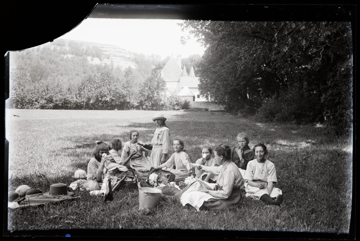 Groupe de jeunes filles pique-niquant à l'ombre des arbres, le château de Chalain en arrière-plan.