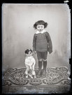 Portrait d'un petit garçon debout accompagné d'un chien qui fait le beau.