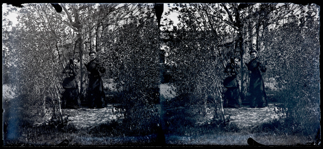 Deux femmes dans un jardin au milieu des arbres, l'une d'elles tient un chat noir dans les bras.