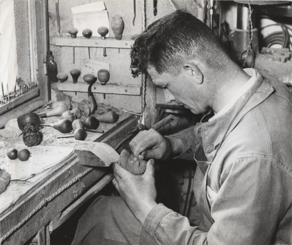 Artisan sculptant une tête d'homme sur une pipe.