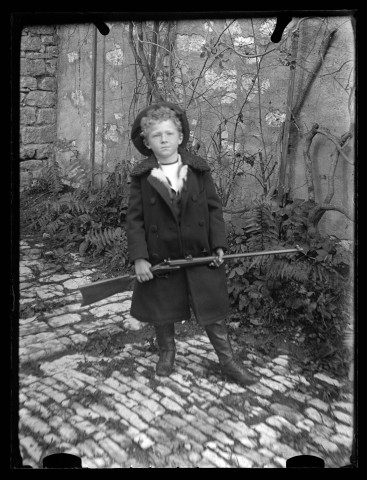 Portrait d'un jeune garçon avec une carabine, vue de face.