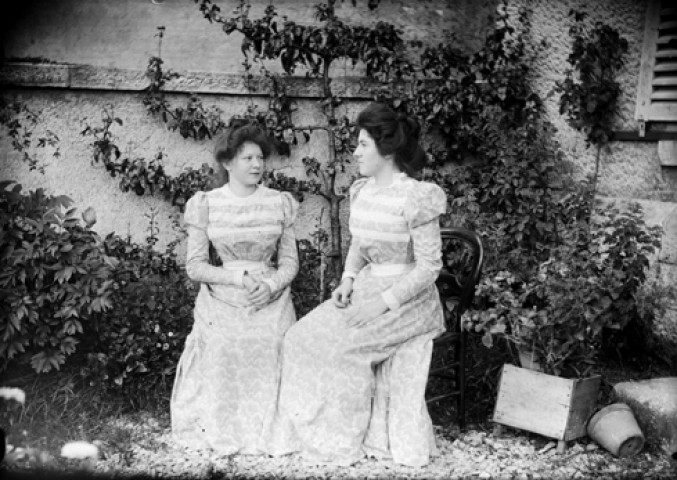 Deux jeunes filles assisent sur des chaises au milieu d'un jardin