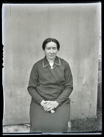 Portrait d'une femme assise portant une robe sombre brodée au niveau de la taille.