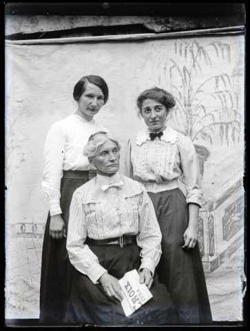 Portrait de deux jeunes femmes debout entourant Agathe Coutemoine assise, devant un décor peint.