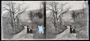 Deux femmes et un chien sur un chemin boueux bordé d'arbres, un village se devine au loin.