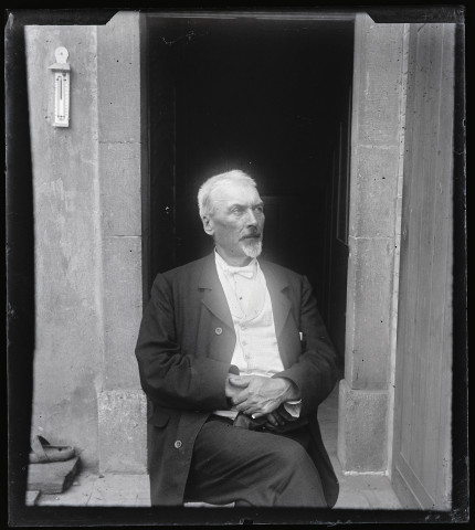 Portrait d'Elisée Coutemoine assis devant une porte ouverte.