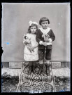 Portrait de deux enfants avec des jouets, la fillette tient une poupée dans les bras, le petit garçon s'appuie sur une carabine.