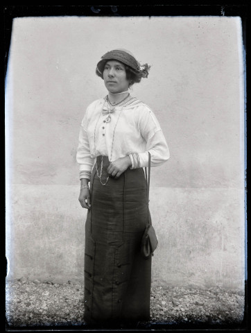Portrait d'une femme debout portant chapeau et sac à main.