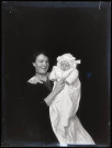 Portrait d'une femme tenant dans ses bras un bébé en tenue de baptême, une tétine à la bouche.