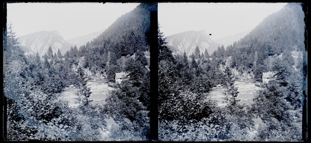 Bâtiment au bord d'un cours d'eau en forêt dans un paysage de montagnes.