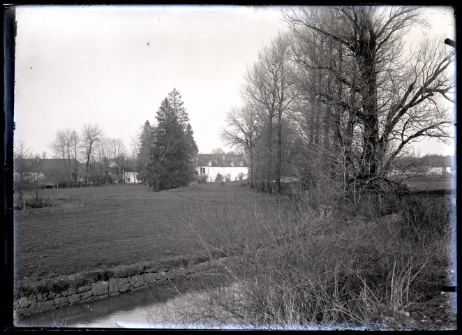 Parc et maisons de Vers-en-Montagne au loin, vue prise près d'un cours d'eau.