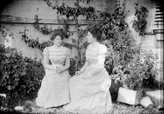 Deux jeunes filles assisent sur des chaises au milieu d'un jardin