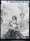 Portrait d'une fillette assise devant un décor peint, une poupée dans les bras.