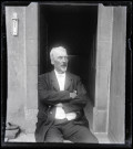 Portrait d'Elisée Coutemoine assis les bras croisés devant une porte ouverte.