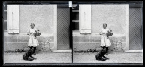 Portrait d'une petite fille tenant un panier dans lequel se trouver un chaton, un chien se couche à ses pieds.