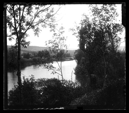 Paysage du Doubs avec un cours d'eau, des arbres et des maisons au loin.