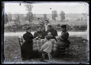 Groupe de femmes jouant aux cartes en extérieur, un jeune garçon est assis sur un cheval à roulettes.