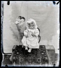 Portrait d'un petit enfant habillé de blanc assis sur une petite chaise, devant une grande peluche de bélier.