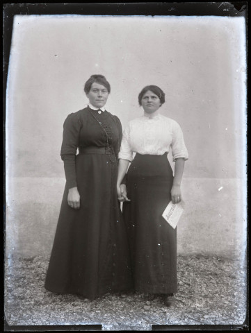 Portrait de deux femmes se donnant la main, l'une tient un journal.