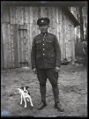 Portraits du Corps des forestiers canadiens et autres troupes : sous-officier canadien tenant un petit chien en laisse devant un baraquement en bois.