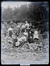 Groupe de femmes et de fillettes assises sur des pierres, un rideau de végétation en arrière-plan, Agathe Coutemoine debout à l'arrière du groupe.