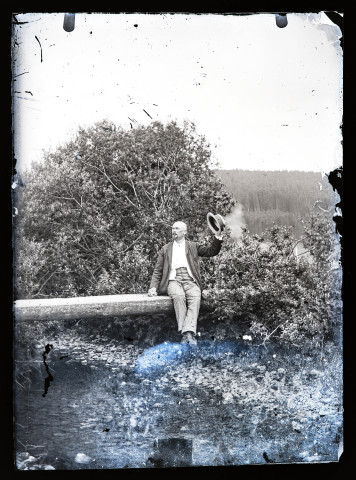 Elisée Coutemoine assis sur un tronc d'arbre servant de passerelle au dessus d'un cours d'eau.