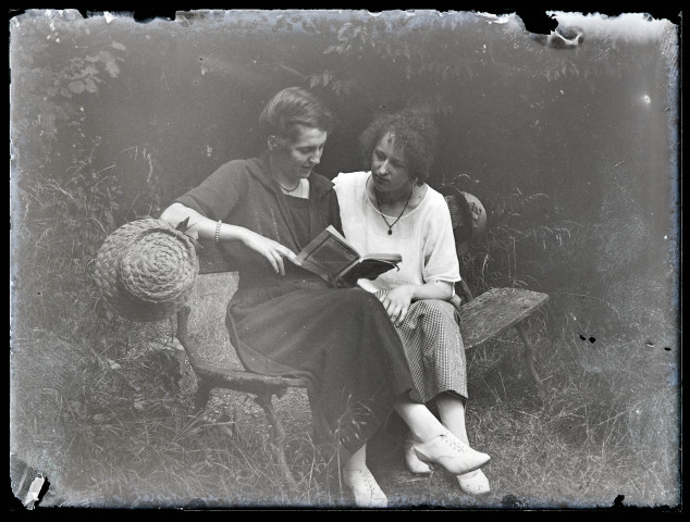 Deux femmes assises sur un banc lisent un livre.