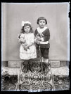Portrait de deux enfants avec des jouets, la fillette tient une poupée dans les bras, le petit garçon s'appuie sur une carabine.