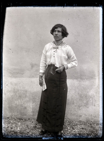 Portrait d'une jeune femme debout, un journal plié à la main.