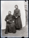 Portrait d'une jeune femme debout derrière un homme en soutane assis.