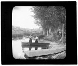 Jeunes filles debout dans une barque amarrée près de Port-Lesney, un groupe de femmes les observe depuis la berge.