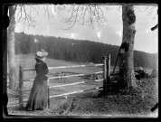 Femme devant une barrière, une forêt au loin.