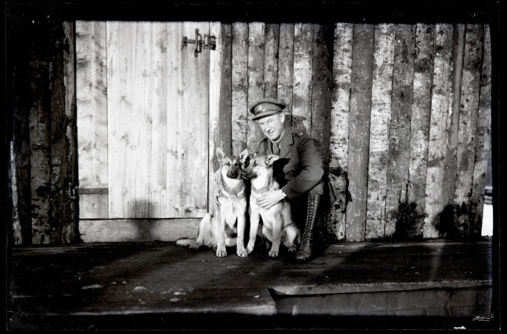 Portraits du Corps des forestiers canadiens et autres troupes : officier du 165e bataillon canadien enlaçant deux chiens devant un baraquement en bois.