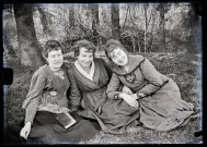 Portrait de trois femmes assises dans l'herbe à l'ombre des arbres, Agathe Rameaux est au centre.