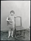 Portrait d'une fillette debout, appuyée à une chaise.