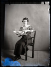 Portrait d'une jeune femme assise, accoudée au dossier de la chaise, une publication ouverte entre les mains.