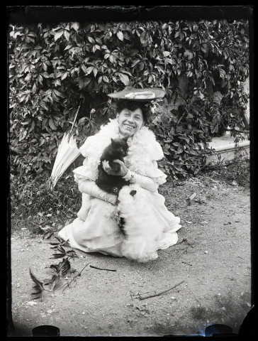 Portrait d'Emilie Vuillaume accroupie, tenant un chat noir dans les bras.